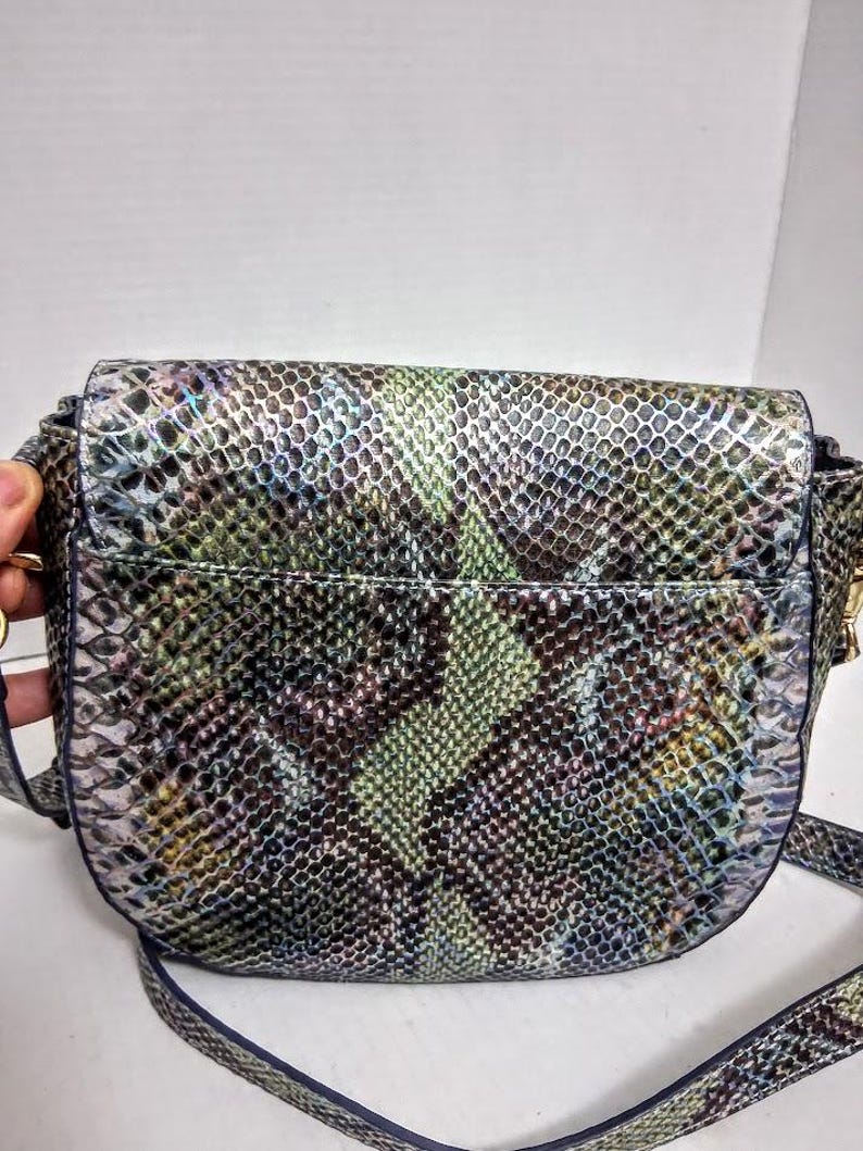 May include: A crossbody bag featuring a textured snakeskin pattern in shades of iridescent green, purple, blue, and black. The bag has a rounded flap closure, a structured silhouette, and a matching adjustable shoulder strap attached to the sides.