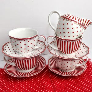 May include: A stacked tea set with red and white polka dots and stripes. The set includes teacups, saucers, and a creamer. The cups and saucers have scalloped edges and a decorative trim.
