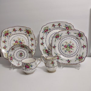 May include: A vintage porcelain tea set featuring a floral pattern with pink, blue, and yellow flowers. The set includes plates, a cup, and a creamer, all with gold trim. The plates are square and round.
