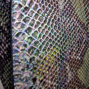 May include: A handbag featuring a textured snakeskin pattern with an iridescent finish. The surface displays a gradient of green, black, and purple hues with a metallic sheen. A gold-toned metal clasp is visible at the bottom right corner.