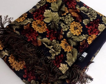 May include: A rectangular throw blanket featuring a dark navy blue background with a repeating pattern of red grapes, green grape leaves, and yellow flowers. The edges of the blanket are finished with long, dark brown fringe trim on two sides.