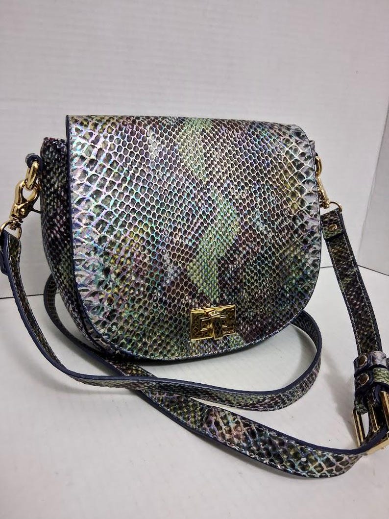 May include: A saddle-shaped crossbody bag featuring an iridescent snakeskin pattern in shades of green, purple, and silver. The bag includes a gold-tone rectangular turn-lock closure on the front flap and an adjustable shoulder strap with gold hardware.