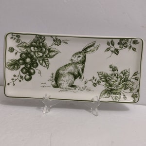 May include: Rectangular ceramic serving dish with a green floral and rabbit design. The dish has a white background with a green border. The design features a rabbit, flowers, and grapes in a detailed, vintage style.