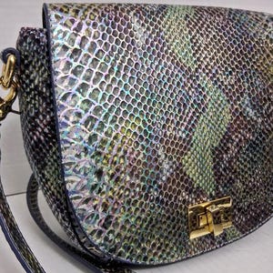May include: A crossbody bag featuring a snakeskin pattern with iridescent hues of blue, green, and purple. The bag has a rounded flap closure secured by a gold-tone metal turn-lock clasp and includes a matching shoulder strap attached with gold hardware.