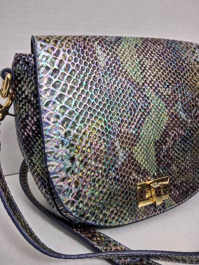 May include: A crossbody bag featuring a snakeskin pattern with iridescent hues of blue, green, and purple. The bag has a rounded flap closure secured by a gold-tone metal turn-lock clasp and includes a matching shoulder strap attached with gold hardware.