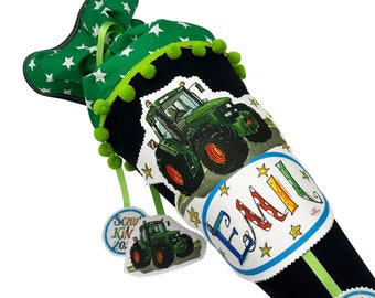 May include: A black school cone with green and white stars, a green ribbon, and a green pom-pom trim. The cone has a tractor design and the name "Emil" on it. There are two smaller tractor tags attached to the cone. One tag says "Schulkönig 20..." and the other tag says "1. Klasse".