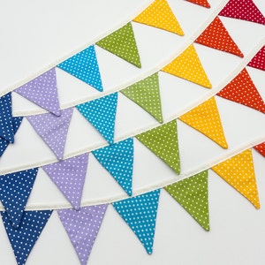 Könnte beinhalten: Eine regenbogenfarbene Girlande mit weißen Punkten. Jede dreieckige Flagge hat eine andere Farbe, beginnend mit Rot und endend mit Blau.