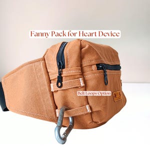 May include: A tan canvas fanny pack for heart device with black zippers, a metal carabiner, and two horizontal fabric loops labeled Belt Loops Option. The text Fanny Pack for Heart Device is visible above the bag.