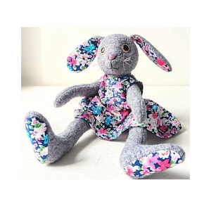 Puede incluir: Una taza de cerámica blanca con asa negra y el texto "But First, Coffee" en negrita negra. La taza se encuentra sobre un fondo borroso, sugiriendo un ambiente acogedor.