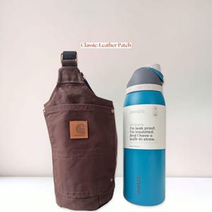 Brown canvas water bottle holder with original leather patch of the Carhartt logo on the back pocket, displayed next to a tall insulated bottle.