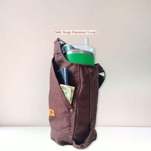 Canvas bottle holder filled with everyday essentials including a handled 40 oz Stanley tumbler, cell phone and money, demonstrating storage capacity and organization.