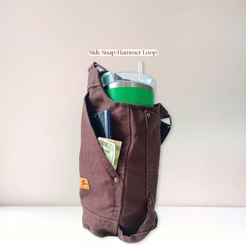 Canvas bottle holder filled with everyday essentials including a handled 40 oz Stanley tumbler, cell phone and money, demonstrating storage capacity and organization.