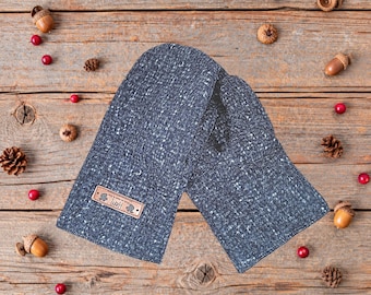 May include: A pair of dark charcoal gray mittens with a speckled white texture. The mittens feature a rectangular brown leather tag on the left side with the text "HART" and a small graphic icon printed in black ink on the surface.