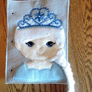 May include: A felt craft depicting a girl with a blue and white crown, blue eyes, and a long white braid. The girl is wearing a light blue dress.