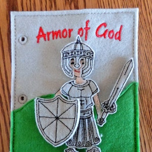 May include: A felt appliqué depicting a knight in armor with a sword and shield. The knight is wearing a helmet and has a red embroidered inscription that reads "Armor of God".