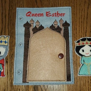 May include: A felt play set with a blue background and a brown door with a brown knob. The text "Queen Esther" is embroidered in red on the blue background. There are two felt figures, a king with a red cape and a queen with a green dress.