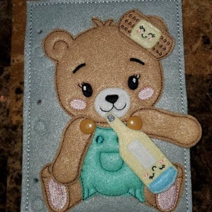 May include: A brown teddy bear wearing a green overall and a bandage on its head is holding a blue and white thermometer. The bear is sitting on a gray felt background.