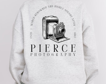 Może przedstawiać: Jasnoszara bluza z ilustracją zabytkowego aparatu fotograficznego i napisem "PIERCE PHOTOGRAPHY" poniżej. Nad aparatem znajduje się napis "ESTD. WORLD-RENOWNED AND HIGHLY SOUGHT AFTER 1883". Bluza wykonana jest z miękkiego materiału.