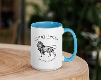 May include: White ceramic mug with a light blue interior and handle. The mug features a black and white illustration of a lion with the words "IMPERTERRITUS" above and "UNDAUNTED | FEARLESS" below the lion.