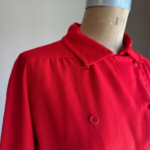 May include: A bright red collared jacket with a double-breasted design. The jacket features a classic collar, long sleeves, and several matching red buttons. The garment is displayed on a mannequin.