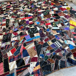 May include: A patchwork quilt with a complex design. The quilt is made of many small, irregularly shaped fabric pieces in various colors, including red, blue, black, and brown. The quilt is lying on a light-colored floor.