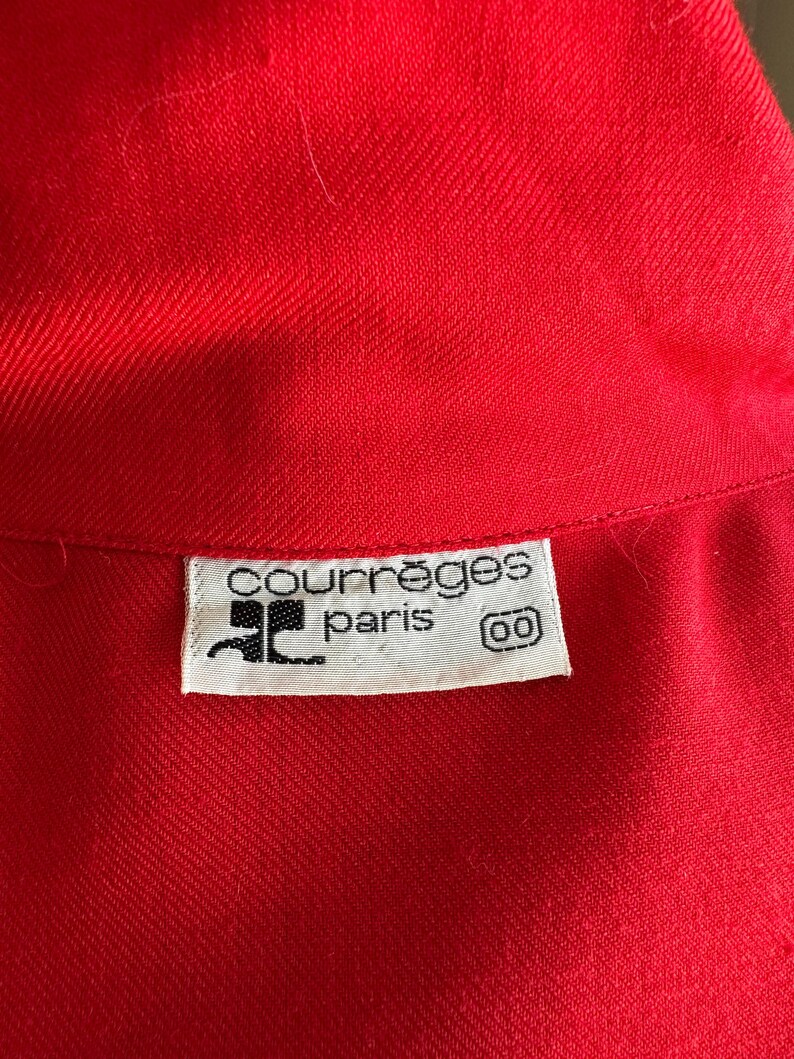 May include: Close-up of a bright red garment with a textured weave. A white label with the text "courr&egrave;ges paris" and a logo is visible. The garment appears to be a piece of clothing.