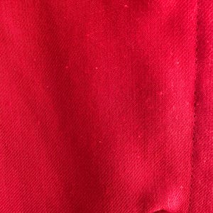 May include: Close-up of a vibrant red fabric with a subtle woven texture. The image shows a portion of a garment, with a button and a seam visible. The fabric's color is consistent throughout the image.
