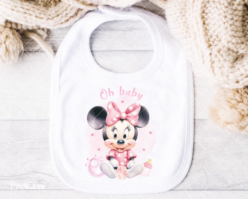 K&ouml;nnte beinhalten: Wei&szlig;es Baby-L&auml;tzchen mit Minnie Mouse-Design. Das L&auml;tzchen hat eine rosa Schleife mit Punkten, ein rosa Outfit und die Worte "Oh baby" in rosa Schrift. Eine Babyflasche und Bl&ouml;cke sind ebenfalls im Design enthalten.