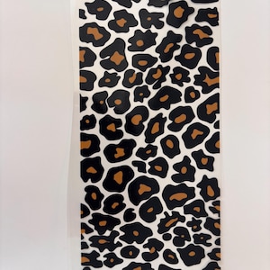 Könnte beinhalten: Ein rechteckiger Aufkleber mit einem sich wiederholenden Leopardenmuster. Das Design besteht aus unregelmäßigen schwarzen Flecken, die mit einer dunkelbraunen Farbe umrandet sind, auf einem weißen Hintergrund. Der Aufkleber hat eine glatte Oberfläche.