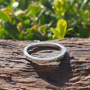 May include: A silver hammered ring with a textured finish. The ring is sitting on a piece of weathered wood.