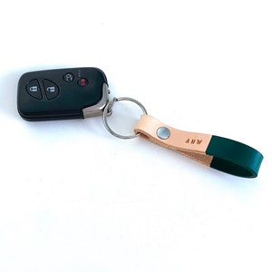 May include: A tan leather keychain with a green leather strap and a silver key ring. The strap has the initials "AMW" embossed on it.