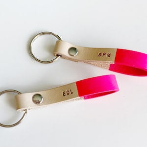 May include: Two leather keychains with a bright pink accent. One keychain has the initials "SPM" and the other has the initials "ECL".
