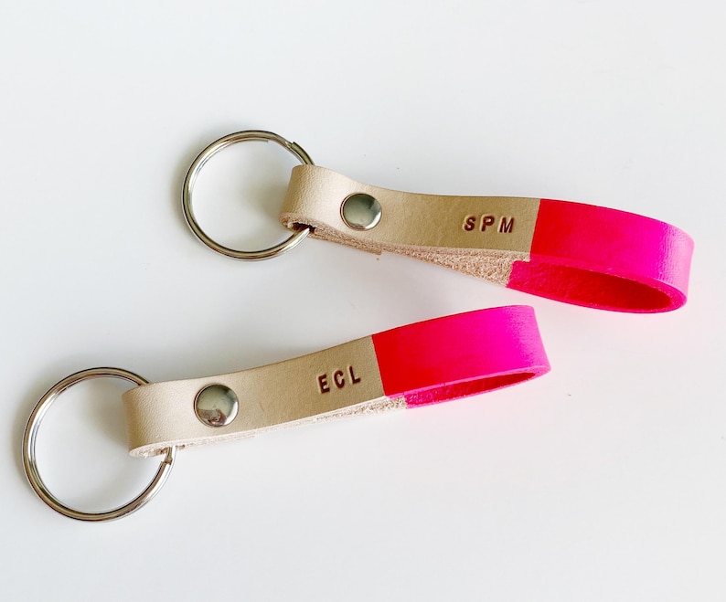 May include: Two leather keychains with a bright pink accent. One keychain has the initials "SPM" and the other has the initials "ECL".