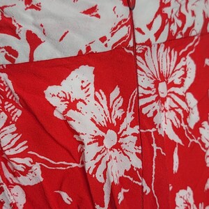 May include: Close-up of a red and white floral print fabric. The fabric features large white flower and leaf patterns against a red background. A zipper is visible along the seam.