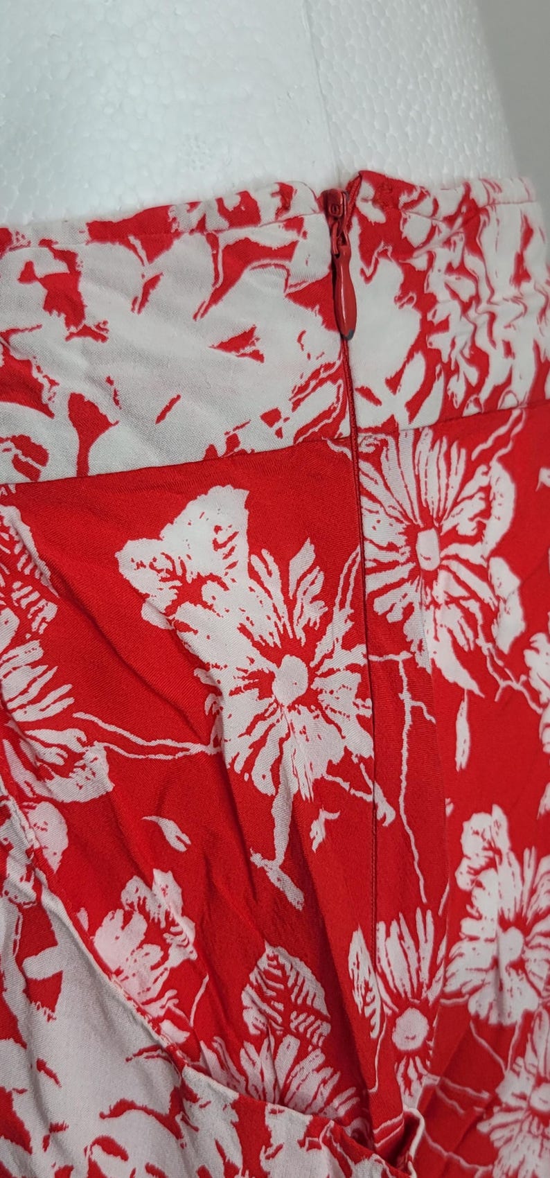 May include: Close-up of a red and white floral print fabric. The fabric features large white flower and leaf patterns against a red background. A zipper is visible along the seam.
