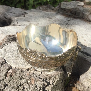 May include: A silver bowl with an ornate design. The bowl is sitting on a tree stump.
