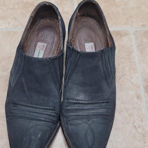 May include: A pair of black suede cowboy boots with pointed toes and decorative stitching. The boots have a pull-on style and a low heel.