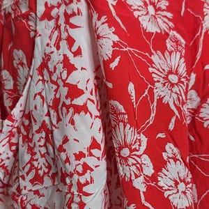 May include: Close-up of a pair of red and white floral print shorts. The shorts feature a high waist and a bold floral pattern. The fabric is lightweight and appears to be cotton or a similar material.