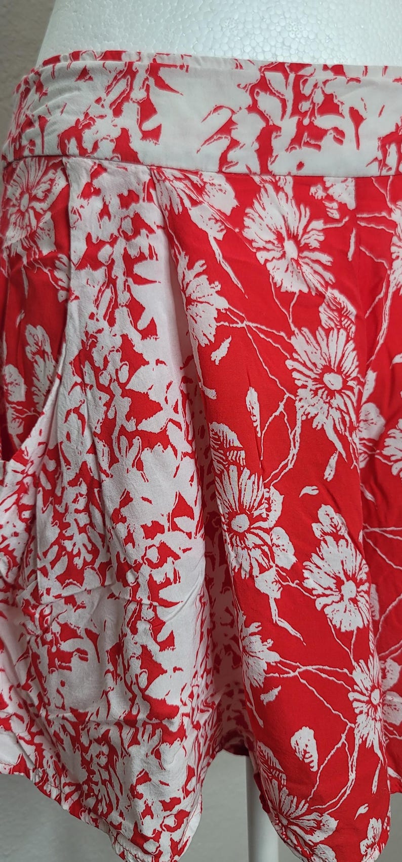 May include: Close-up of a pair of red and white floral print shorts. The shorts feature a high waist and a bold floral pattern. The fabric is lightweight and appears to be cotton or a similar material.