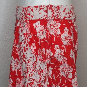 May include: A red skirt with a white floral pattern. The skirt is knee-length and has a wide waistband. The floral design is a repeating pattern of large flowers and leaves.