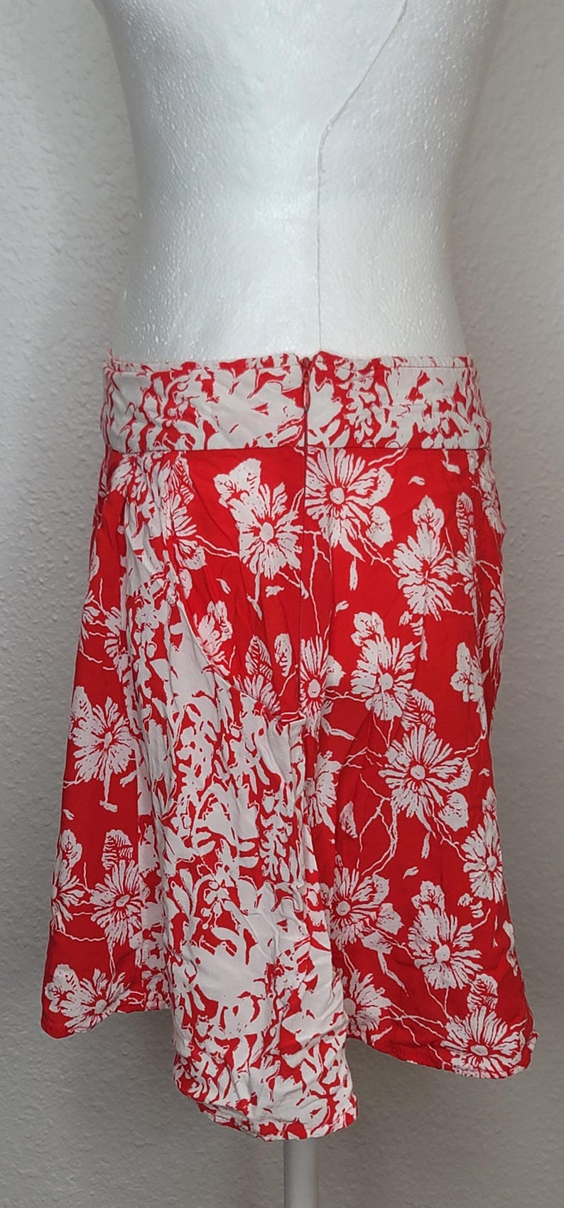May include: A red skirt with a white floral pattern. The skirt is knee-length and has a wide waistband. The floral design is a repeating pattern of large flowers and leaves.