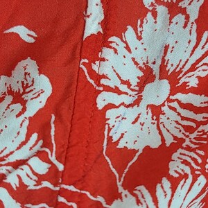 May include: Close-up of red fabric with a white floral pattern. The design features large, stylized flowers and leaves. The fabric is likely used for clothing or home decor.