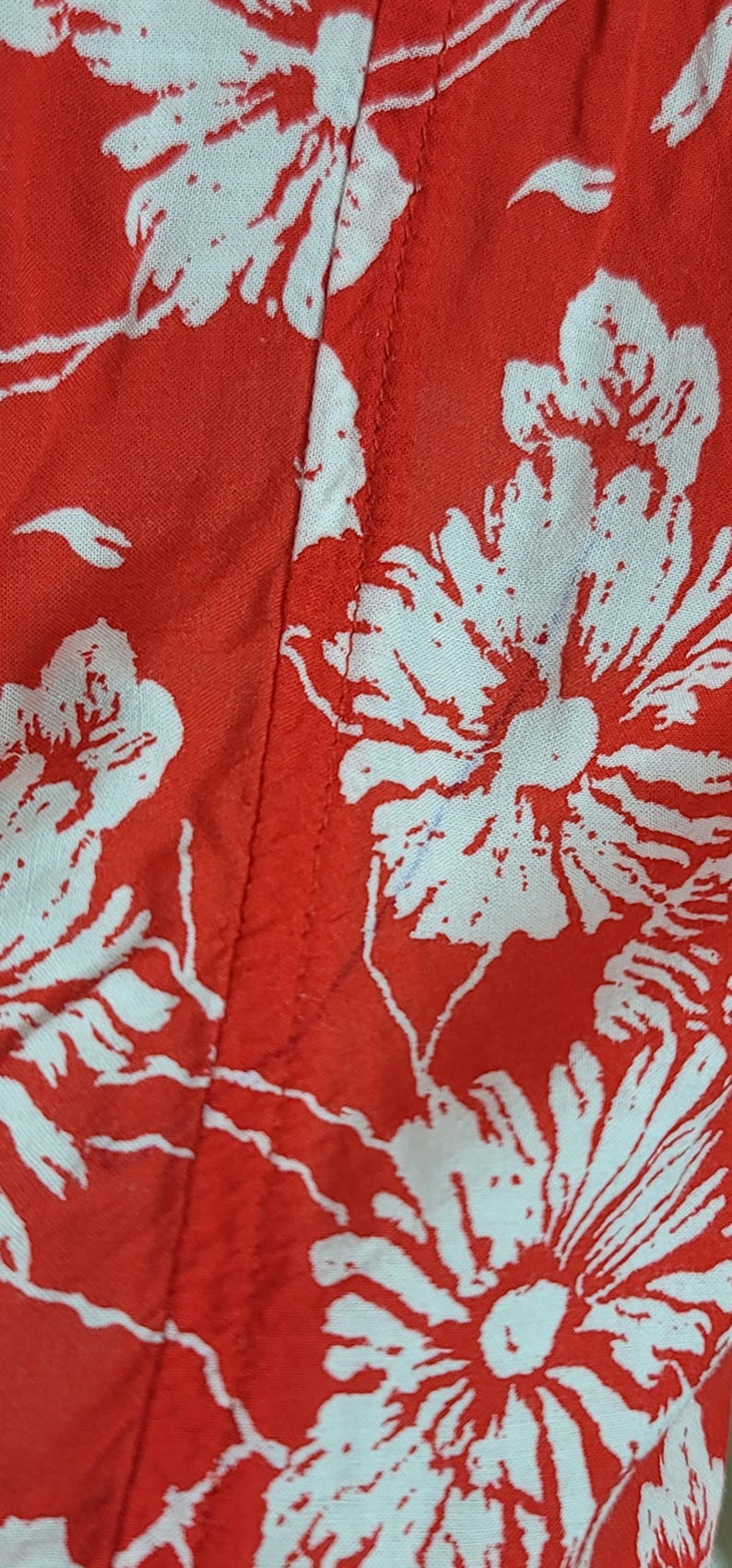 May include: Close-up of red fabric with a white floral pattern. The design features large, stylized flowers and leaves. The fabric is likely used for clothing or home decor.