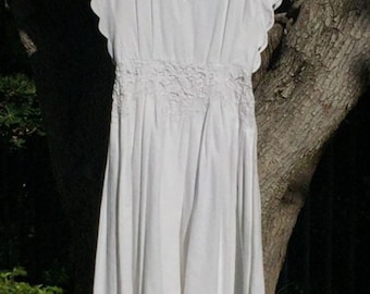 May include: A white cotton dress with lace detailing around the neckline, sleeves, and hem. The dress has a fitted bodice and a flowing skirt.