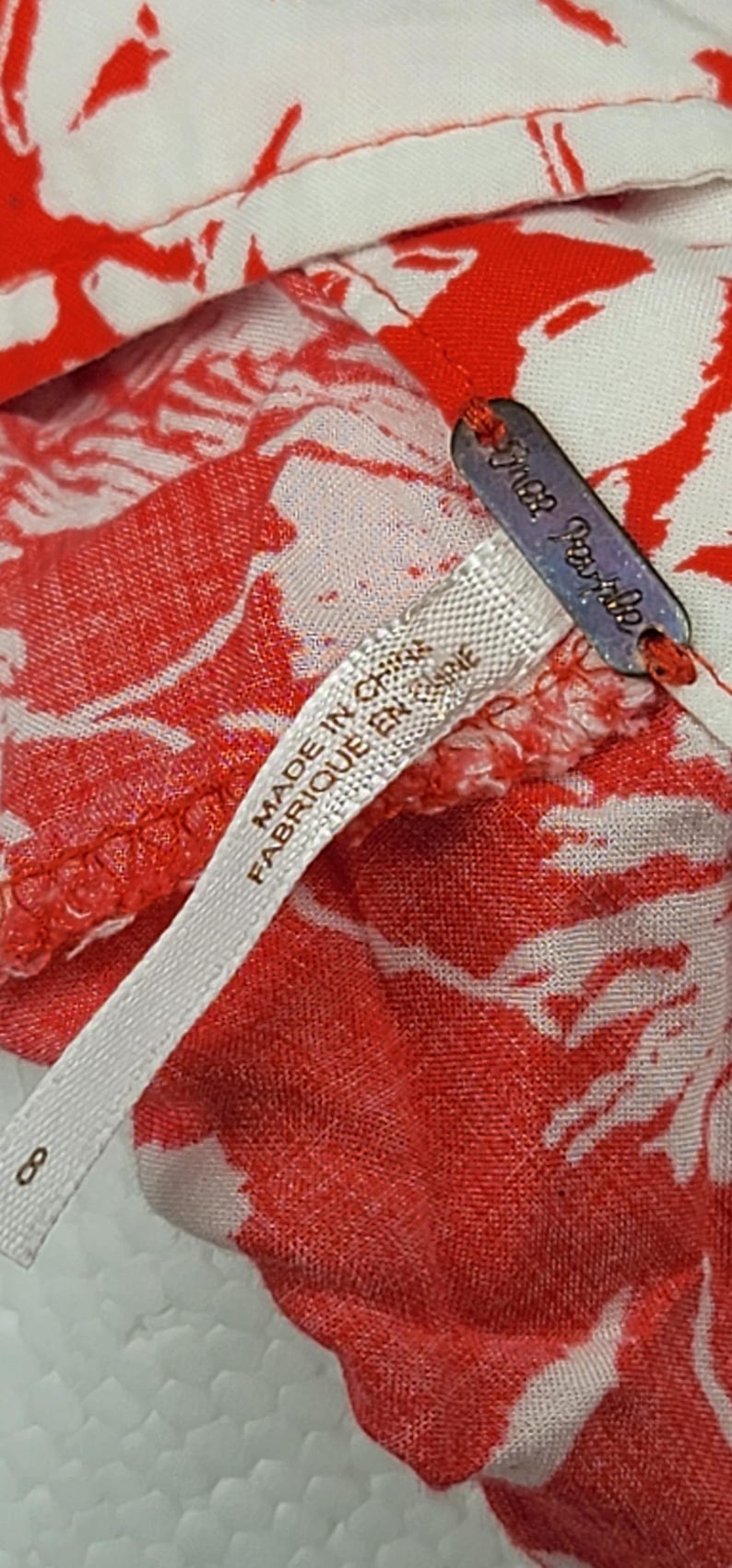 May include: Close-up of a red and white floral patterned fabric. The fabric has a tag that says "Free People" and a label that says "MADE IN CHINA FABRIQUE EN CHINE". The number "8" is also visible.