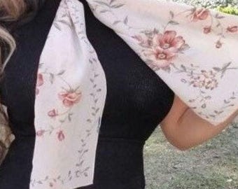 May include: A light pink floral scarf with a delicate floral pattern. The scarf is tied around the neck in a loose knot.