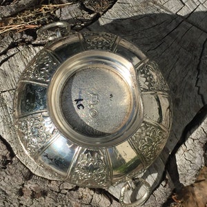 May include: Silver bowl with an ornate floral design and two handles. The bottom of the bowl has the number "250" inscribed on it.