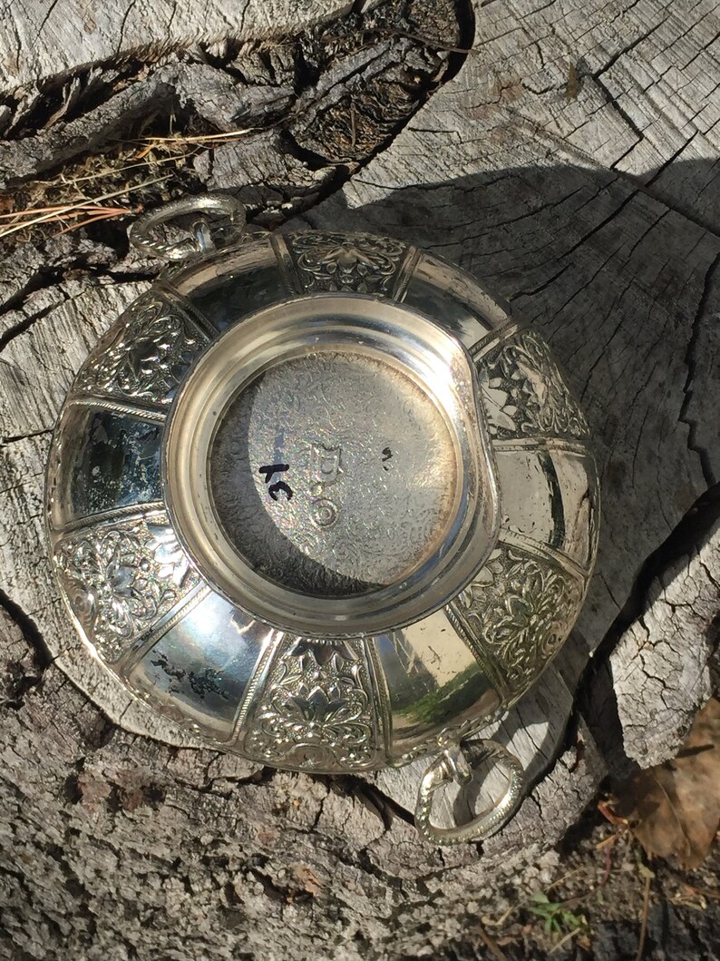 May include: Silver bowl with an ornate floral design and two handles. The bottom of the bowl has the number "250" inscribed on it.