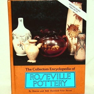 Può includere: La copertina del libro The Collectors Encyclopedia of Roseville Pottery presenta una collezione di pezzi di ceramica vintage in vari colori e design. La copertina del libro è arancione con un titolo blu.
