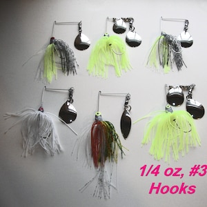 May include: A selection of fishing lures with shiny silver blades and vibrant skirts. The lures display a range of colours, including white, grey, red, green, and neon yellow. The image includes the text "1/4 oz, #3 Hooks."